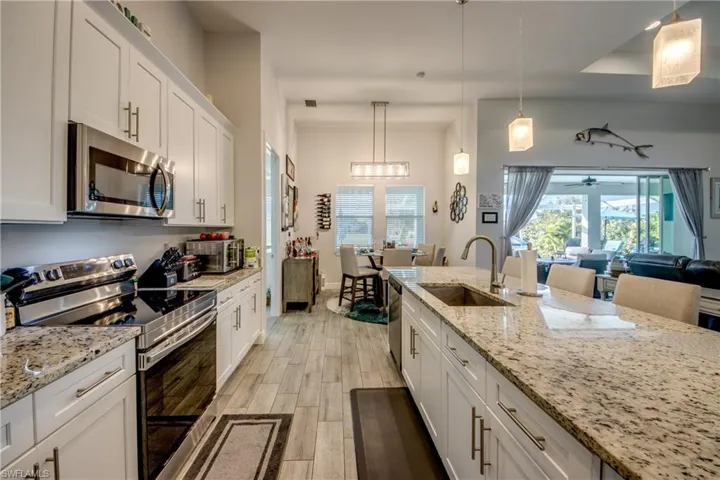 Kitchen with stainless steel appliances, white cabinetry, wood finish floors, and hanging light fixtures