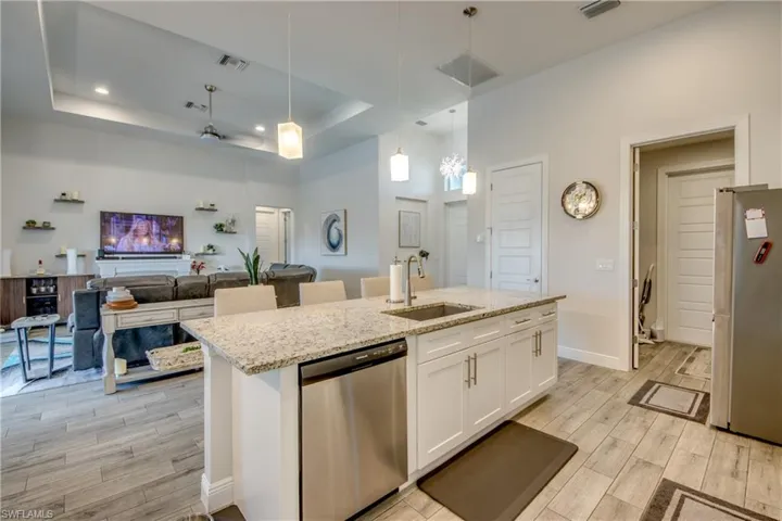 Kitchen featuring a raised ceiling, wood tiled floors, open floor plan, stainless steel appliances, and light stone counters