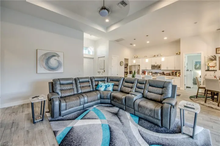 Living area with a tray ceiling, light wood-type flooring, a ceiling fan, and recessed lighting
