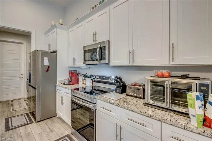 Kitchen featuring stainless steel appliances, white cabinets, light stone countertops, and wood finish floors