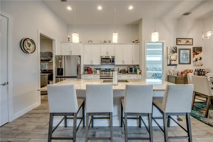 Kitchen with white cabinetry, stainless steel appliances, a kitchen island with sink, wood tiled floors, and a high ceiling