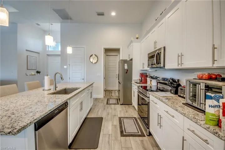 Kitchen with stainless steel appliances, white cabinets, wood finish floors, light stone counters, and hanging light fixtures