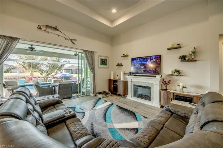 Living area with a high tray ceiling, a ceiling fan, wood finished floors, a glass covered fireplace, and recessed lighting