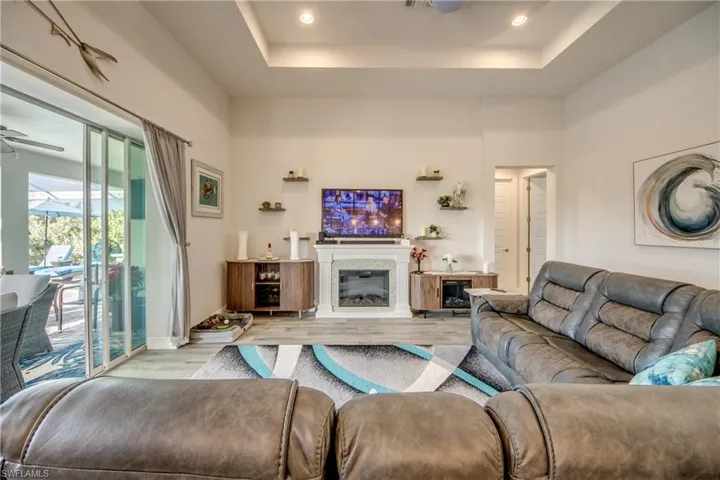 Living room with a ceiling fan, wood finished floors, a high tray ceiling, a glass covered fireplace, and recessed lighting