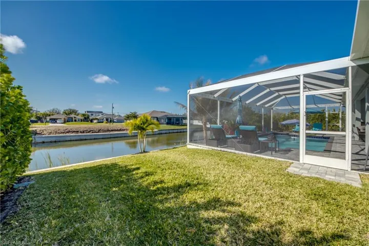 View of grassy yard featuring glass enclosure, a sunroom, an outdoor pool, a water view, and a residential view