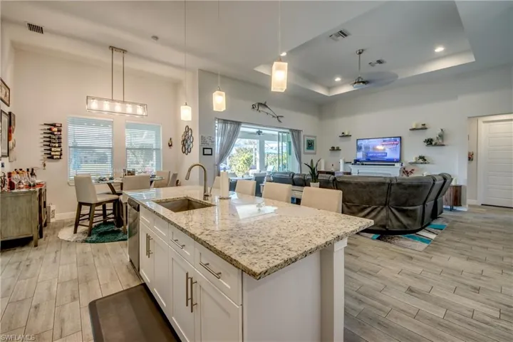 Kitchen featuring open floor plan, wood finish floors, light stone countertops, white cabinetry, and a tray ceiling