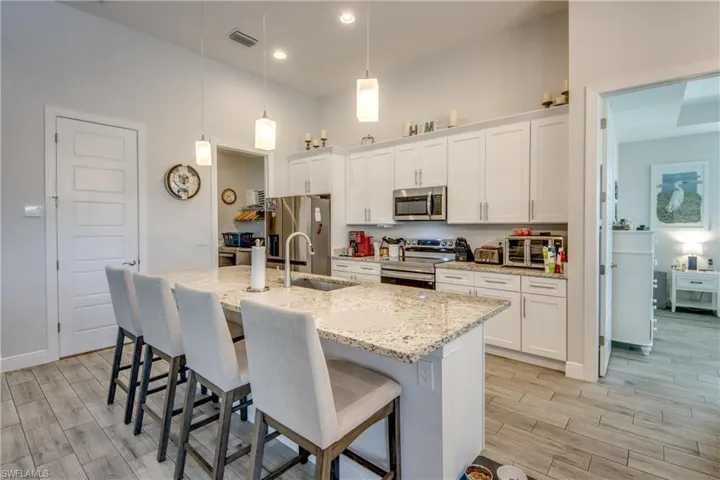 Kitchen featuring white cabinetry, a kitchen breakfast bar, light stone countertops, a kitchen island with sink, and stainless steel appliances