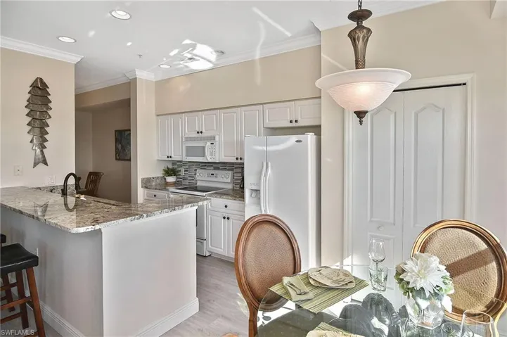 Kitchen featuring tasteful backsplash, light stone countertops, white appliances, crown molding, and white cabinetry
