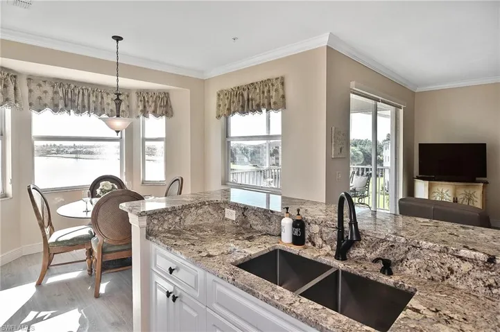 Kitchen with white cabinetry, ornamental molding, light stone countertops, decorative light fixtures, and light wood finished floors