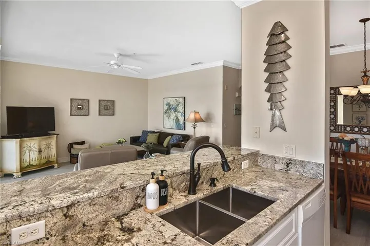 Kitchen with crown molding, open floor plan, light stone countertops, dishwasher, and white cabinetry