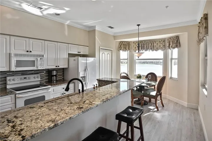 Kitchen featuring light stone counters, ornamental molding, white cabinets, white appliances, and pendant lighting