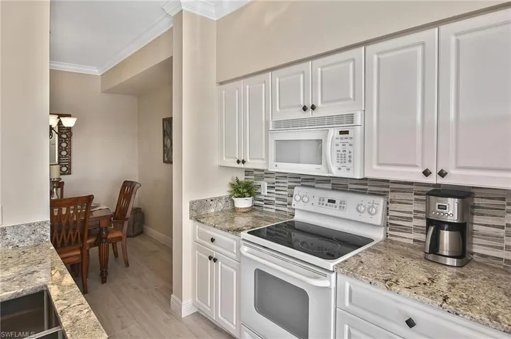 Kitchen with white appliances, white cabinets, light stone counters, ornamental molding, and tasteful backsplash