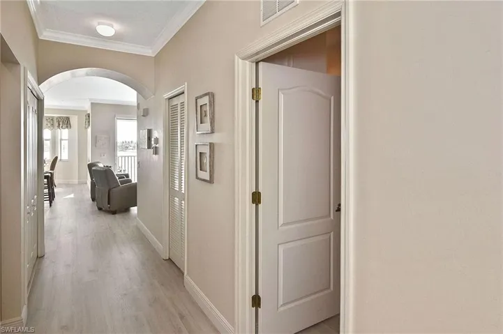 Hall featuring arched walkways, ornamental molding, and light wood-type flooring