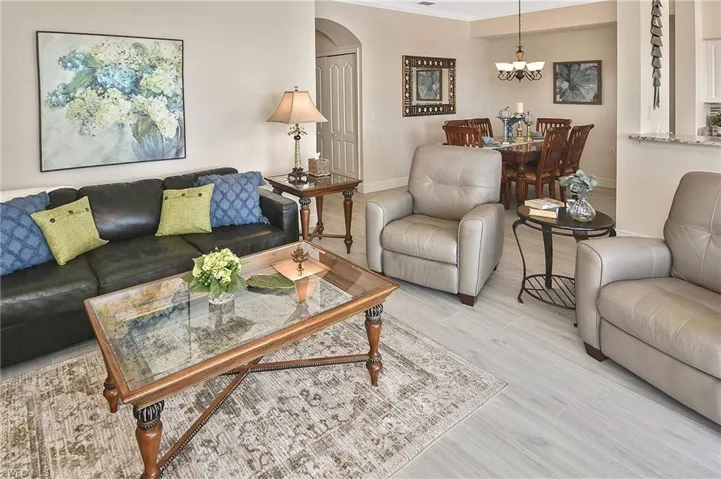 Living area with arched walkways, light wood-style flooring, ornamental molding, and a chandelier