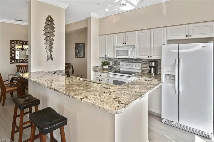 Kitchen with white appliances, white cabinets, backsplash, crown molding, and light stone counters