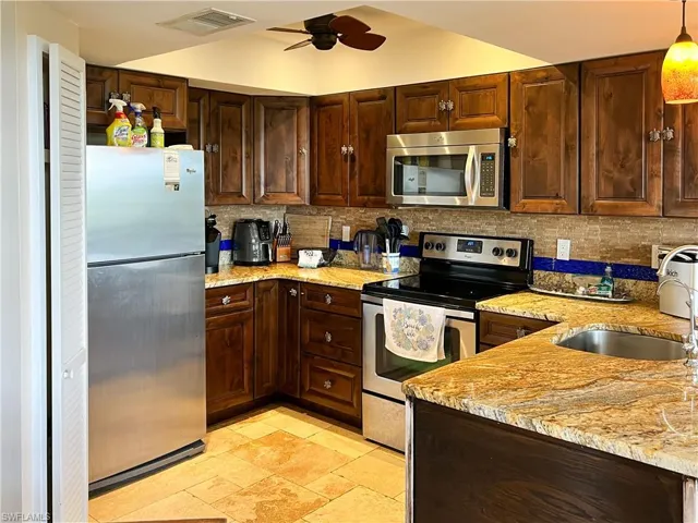 Kitchen with appliances with stainless steel finishes, sink, decorative backsplash, ceiling fan, and light stone counters