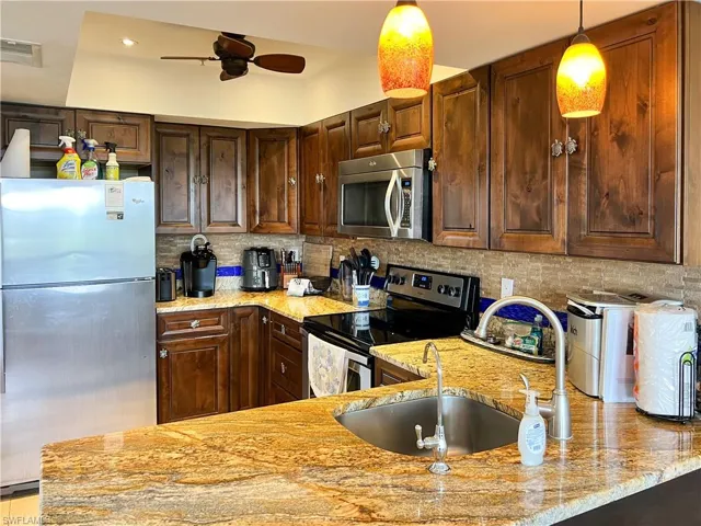 Kitchen with backsplash, ceiling fan, light stone countertops, and appliances with stainless steel finishes