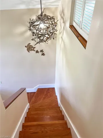 Stairs with wood-type flooring and an inviting chandelier