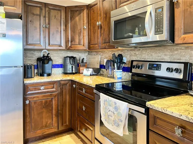 Kitchen with appliances with stainless steel finishes, light stone counters, and decorative backsplash
