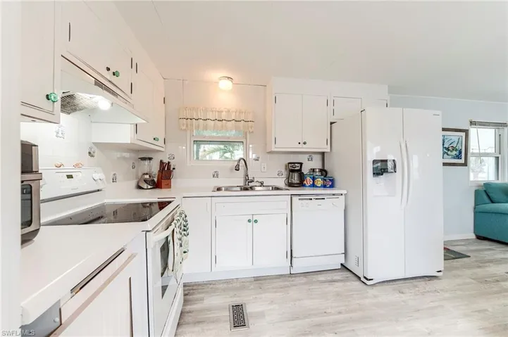 Kitchen featuring white appliances, light countertops, under cabinet range hood, white cabinetry, and light wood-style flooring