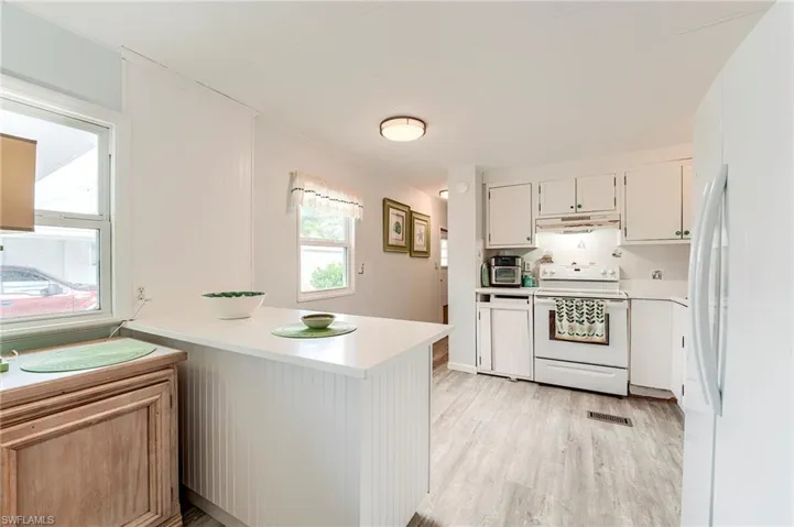Kitchen with white appliances, light countertops, a peninsula, light wood-style flooring, and white cabinetry