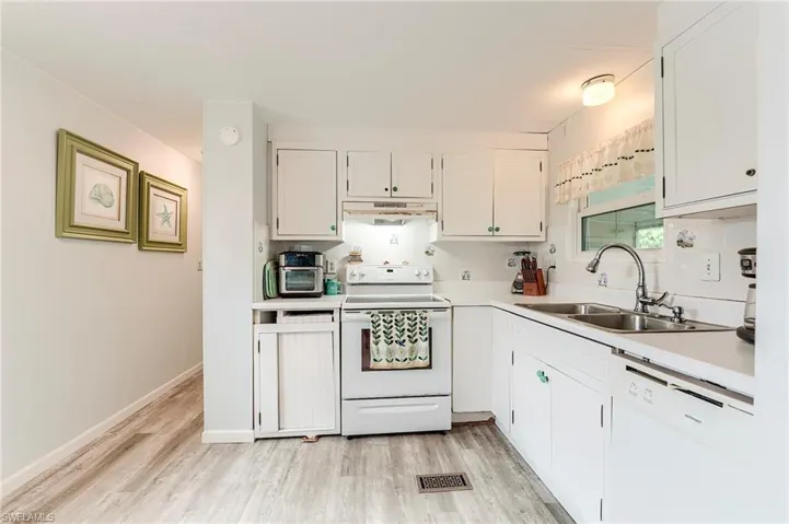 Kitchen featuring white appliances, light countertops, white cabinetry, light wood-style flooring, and under cabinet range hood