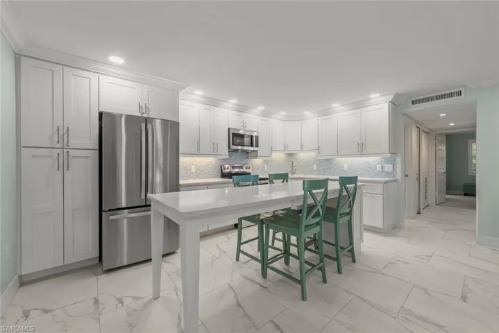 Kitchen featuring appliances with stainless steel finishes, crown molding, white cabinets, light marble finish flooring, and backsplash