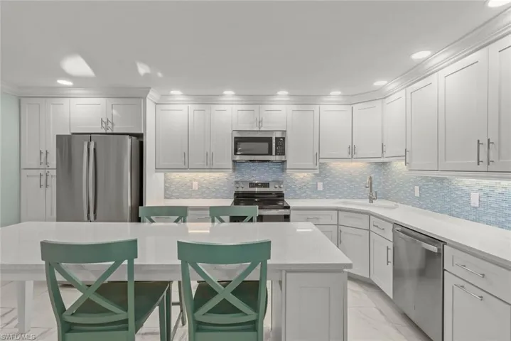 Kitchen featuring stainless steel appliances, light marble finish flooring, a kitchen island, a kitchen bar, and light stone counters