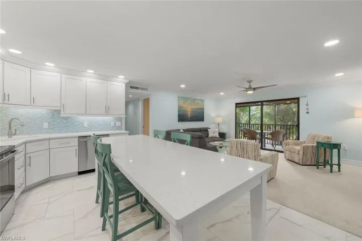 Kitchen with white cabinets, a kitchen breakfast bar, light stone countertops, appliances with stainless steel finishes, and open floor plan