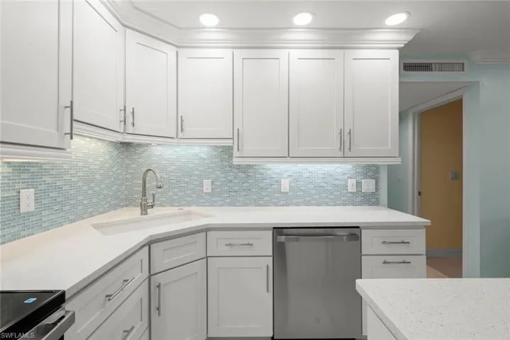 Kitchen with appliances with stainless steel finishes, light stone counters, white cabinetry, decorative backsplash, and recessed lighting