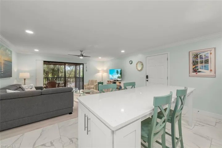 Kitchen featuring light marble finish flooring, white cabinetry, a breakfast bar, ornamental molding, and light stone counters