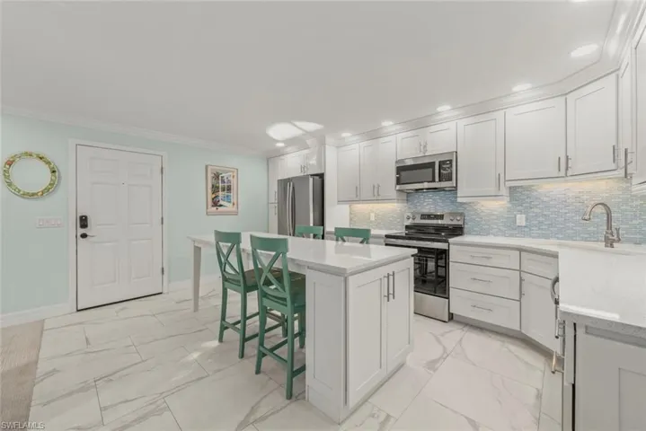 Kitchen featuring appliances with stainless steel finishes, light marble finish flooring, a kitchen breakfast bar, a center island, and crown molding