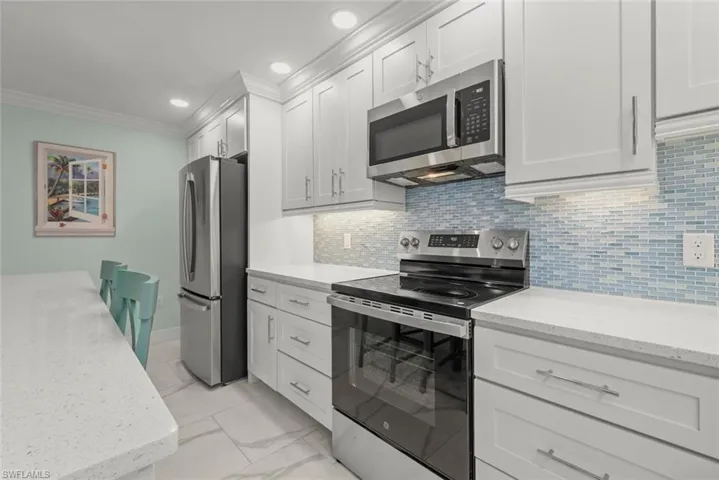 Kitchen featuring appliances with stainless steel finishes, light stone counters, light marble finish floors, white cabinetry, and ornamental molding