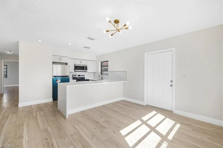 Kitchen with light countertops, a chandelier, appliances with stainless steel finishes, a peninsula, and light wood-style floors