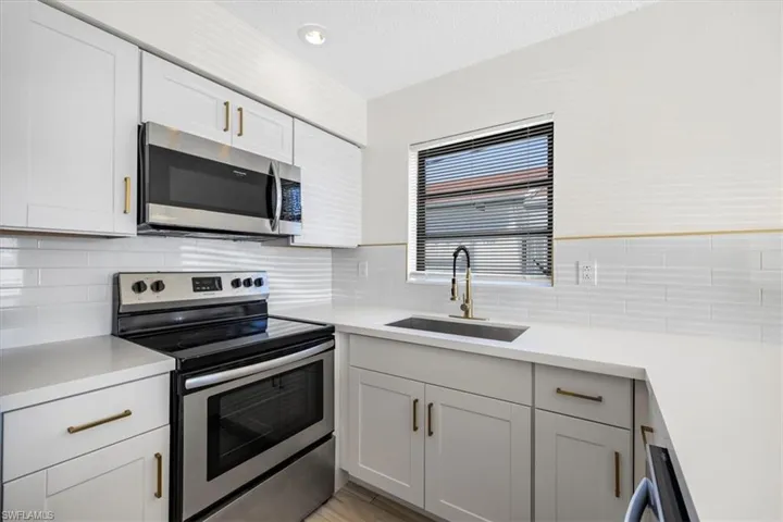 Kitchen featuring a textured ceiling, light countertops, appliances with stainless steel finishes, a sink, and backsplash