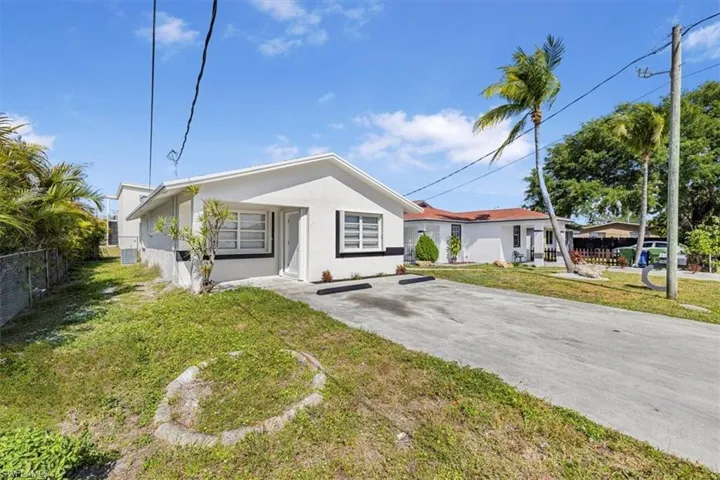 View of front of home featuring stucco siding, driveway, fence, and a front lawn
