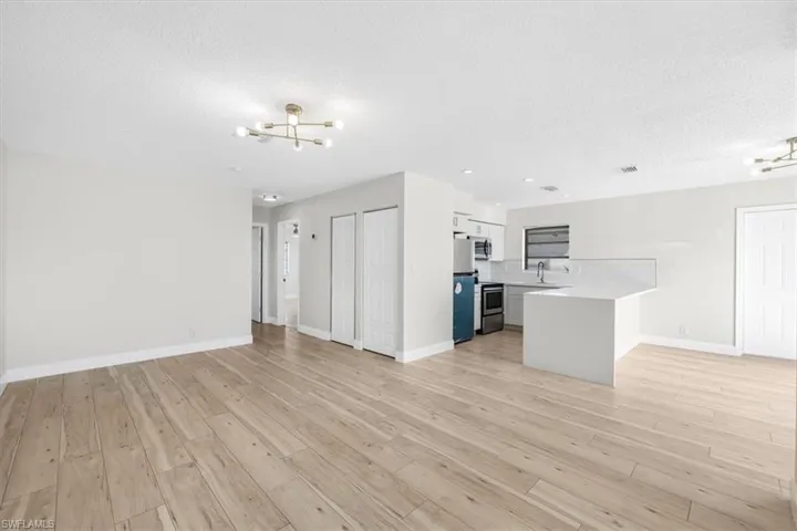 Unfurnished living room with a textured ceiling, light wood-type flooring, a sink, and an inviting chandelier