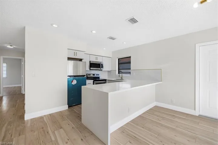 Kitchen with visible vents, a peninsula, stainless steel appliances, a sink, and light wood-style floors