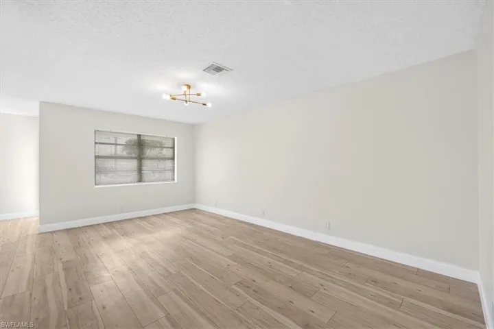 Empty room featuring a textured ceiling, visible vents, light wood finished floors, baseboards, and a notable chandelier