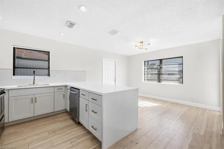 Kitchen featuring stainless steel dishwasher, a sink, light wood finished floors, visible vents, and a peninsula