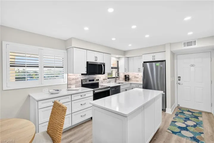 Kitchen with white cabinets, stainless steel appliances, a kitchen island, recessed lighting, and light stone countertops