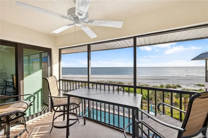 Sunroom / solarium featuring ceiling fan, view of water and beach, a balcony, and carpet floors