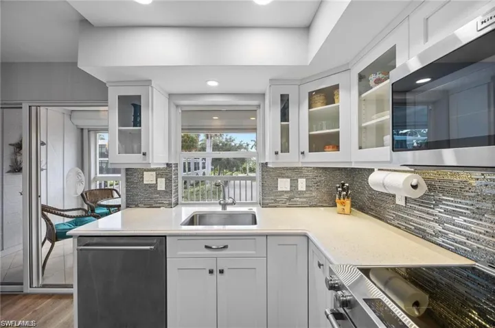 Updated kitchen featuring white cabinetry, solid-surface countertops, stainless steel appliances, and views toward the screened lanai.