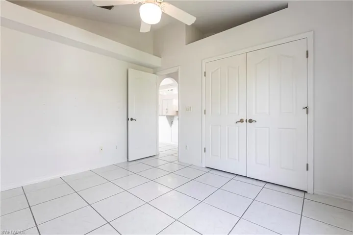 Unfurnished bedroom featuring lofted ceiling, light tile patterned floors, a closet, arched walkways, and a ceiling fan