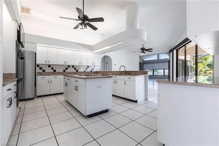 Kitchen featuring ceiling fan, tasteful backsplash, white cooktop, a peninsula, and a kitchen island