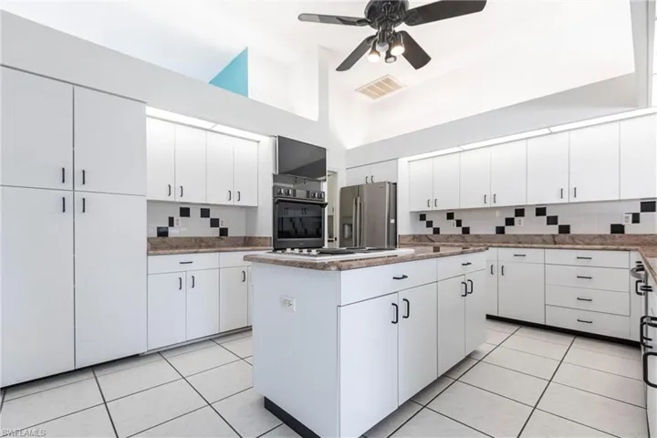 Kitchen with stainless steel appliances, high vaulted ceiling, a center island, a ceiling fan, and backsplash