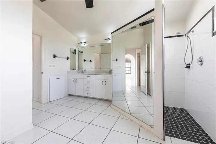 Bathroom featuring double vanity, tiled shower, and tile patterned flooring