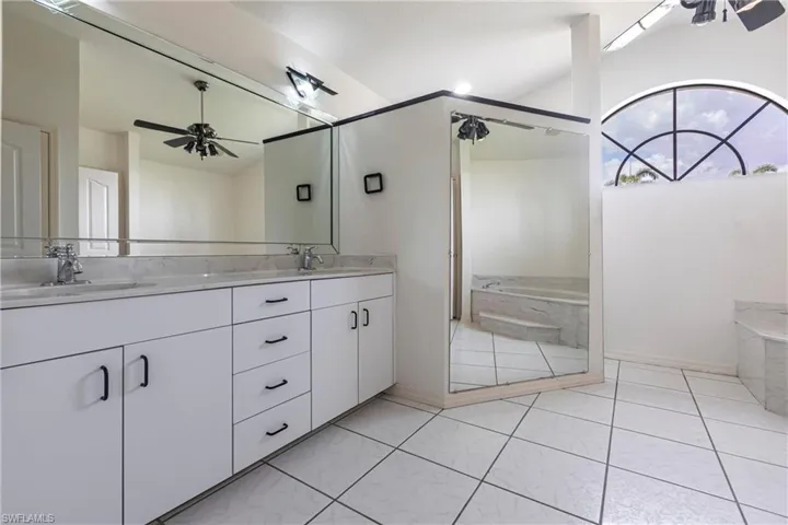 Bathroom featuring a ceiling fan, double vanity, a garden tub, tile patterned floors, and vaulted ceiling