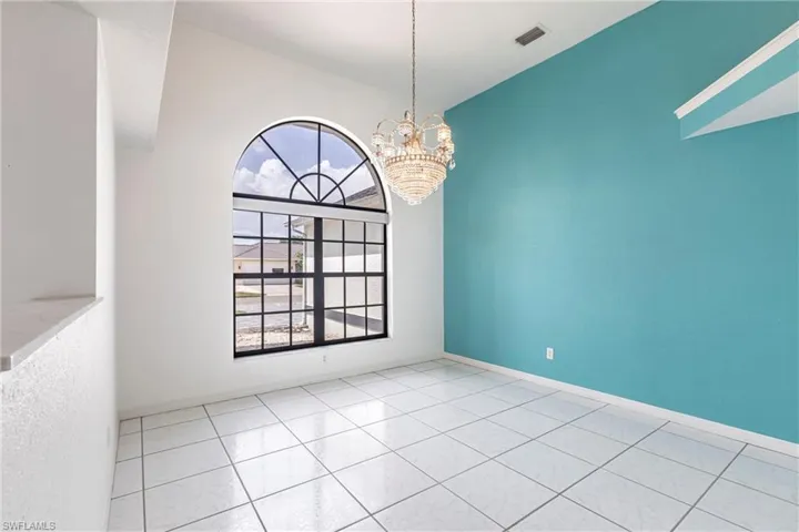 Tiled empty room with a chandelier and baseboards