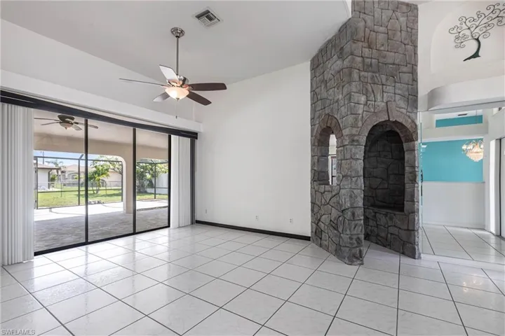 Unfurnished living room featuring ceiling fan, light tile patterned floors, a fireplace, and a towering ceiling